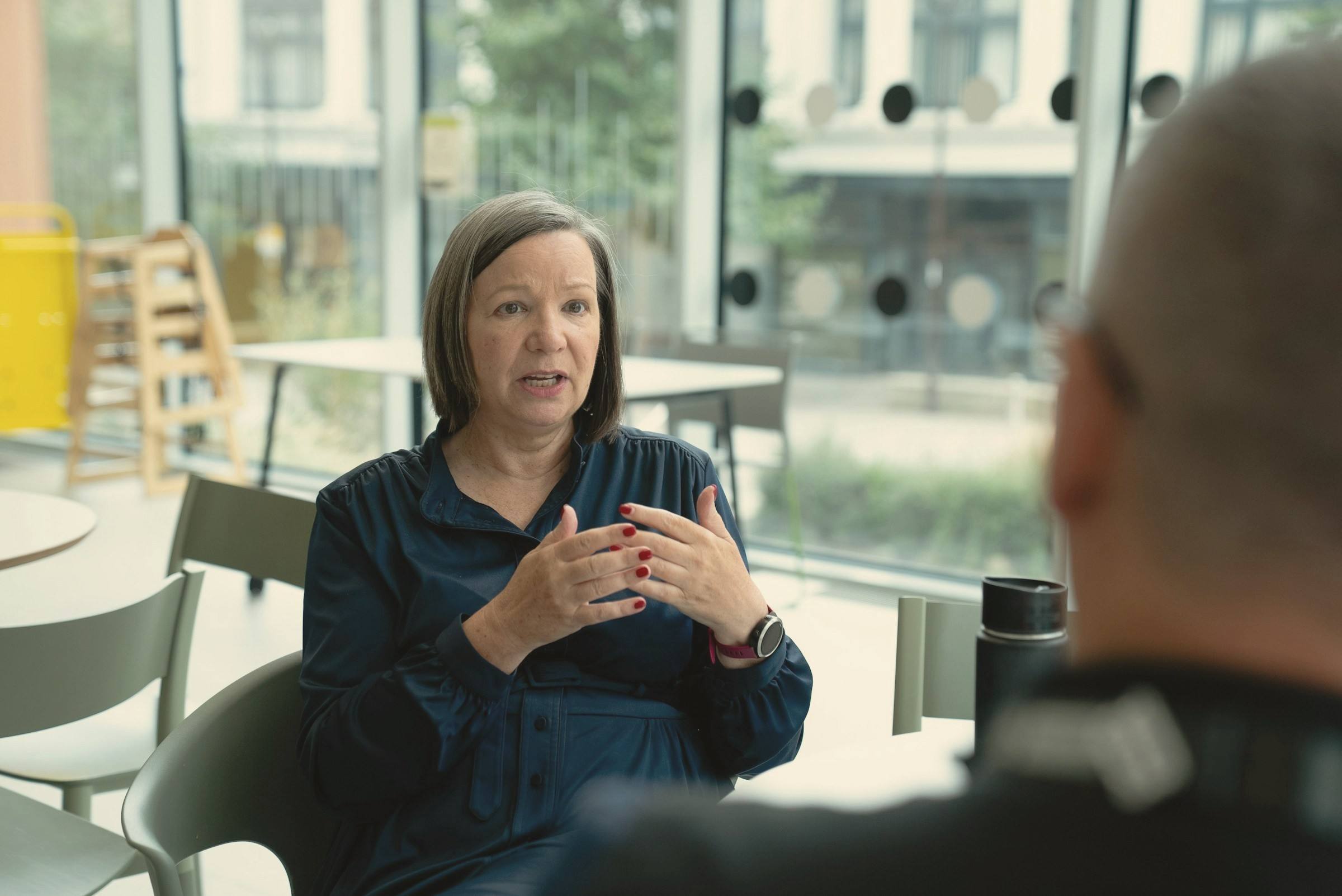 Over-the-shoulder view of a woman explaining her thinking to an interviewer across a table.