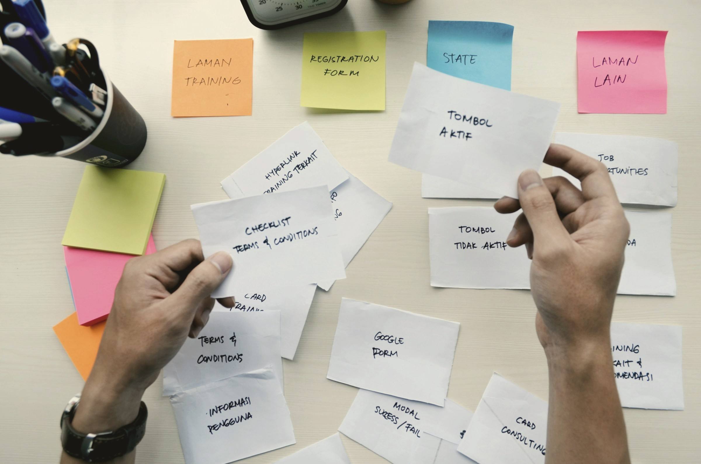Hands sorting handwritten cards and sticky notes into groups on a desk.